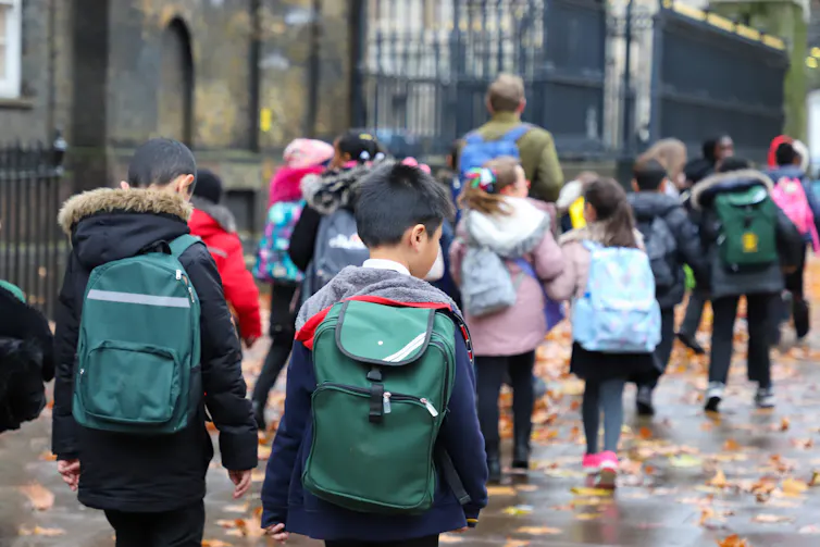 View from behind of a group of primary school children walking down a rainy street