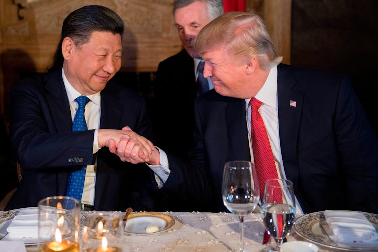 Donald Trump and Xi Jinping sat at a table shaking hands.