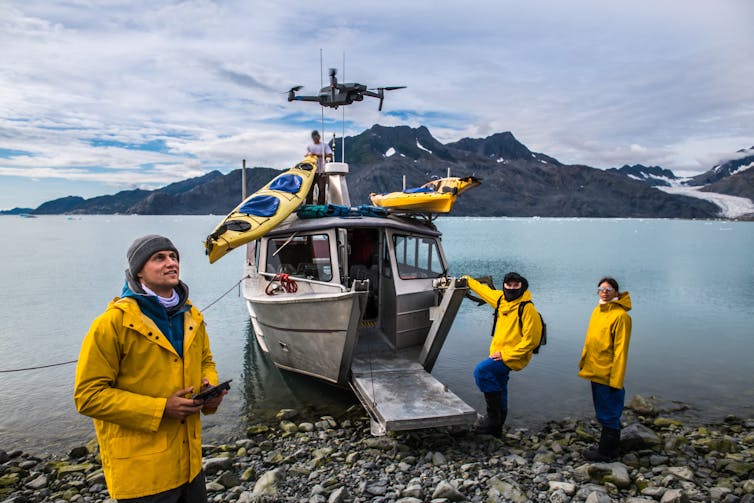 Des chercheurs en cirets jaunes pilotent un drone à côté d’un navire de recherche amarré