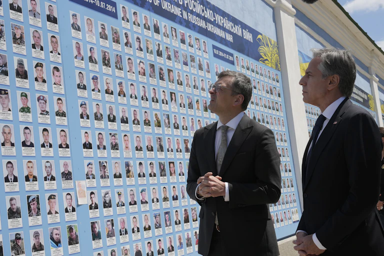 Two men in suits look at a large mural features the faces of fallen soldiers.