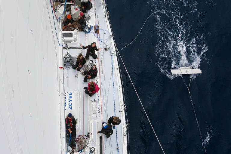 Shot from top of mast looking down onto sailboat, sea to right with trawling white equipment