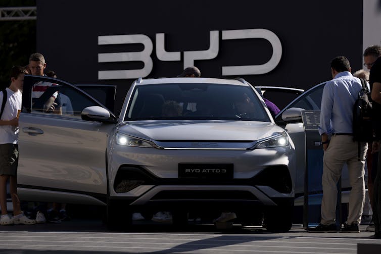 People look in the open doors of a sedan with the letters BYD on the wall behind it.