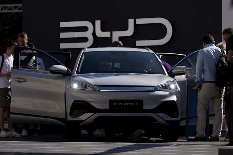 People look in the open doors of a sedan with the letters BYD on the wall behind it.