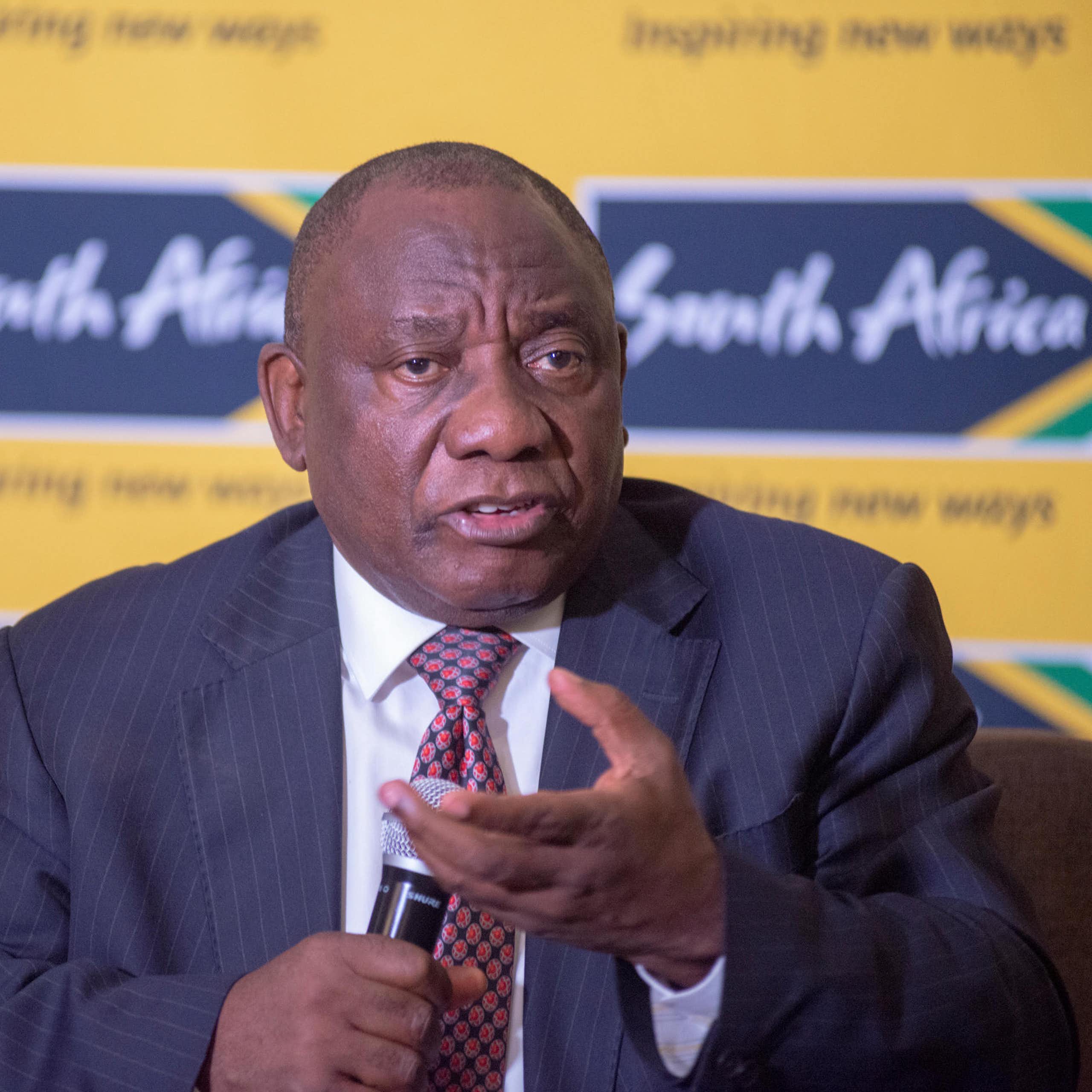 South African president Cyril Ramaphosa in front of South African flags.