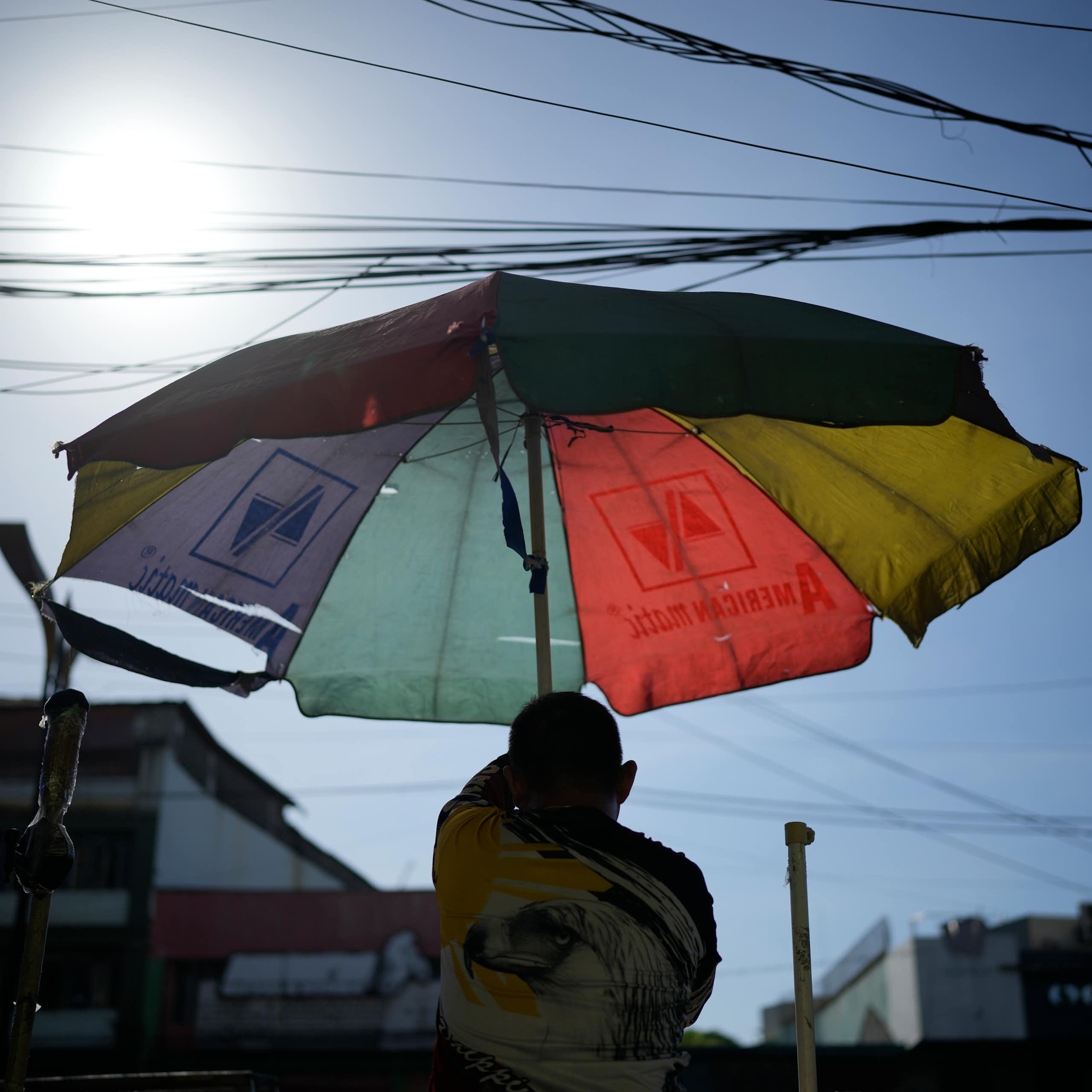 A man hoists an umbrella under a beating sun.