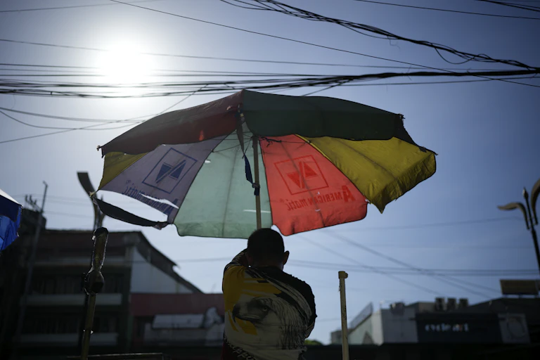 A man hoists an umbrella under a beating sun.