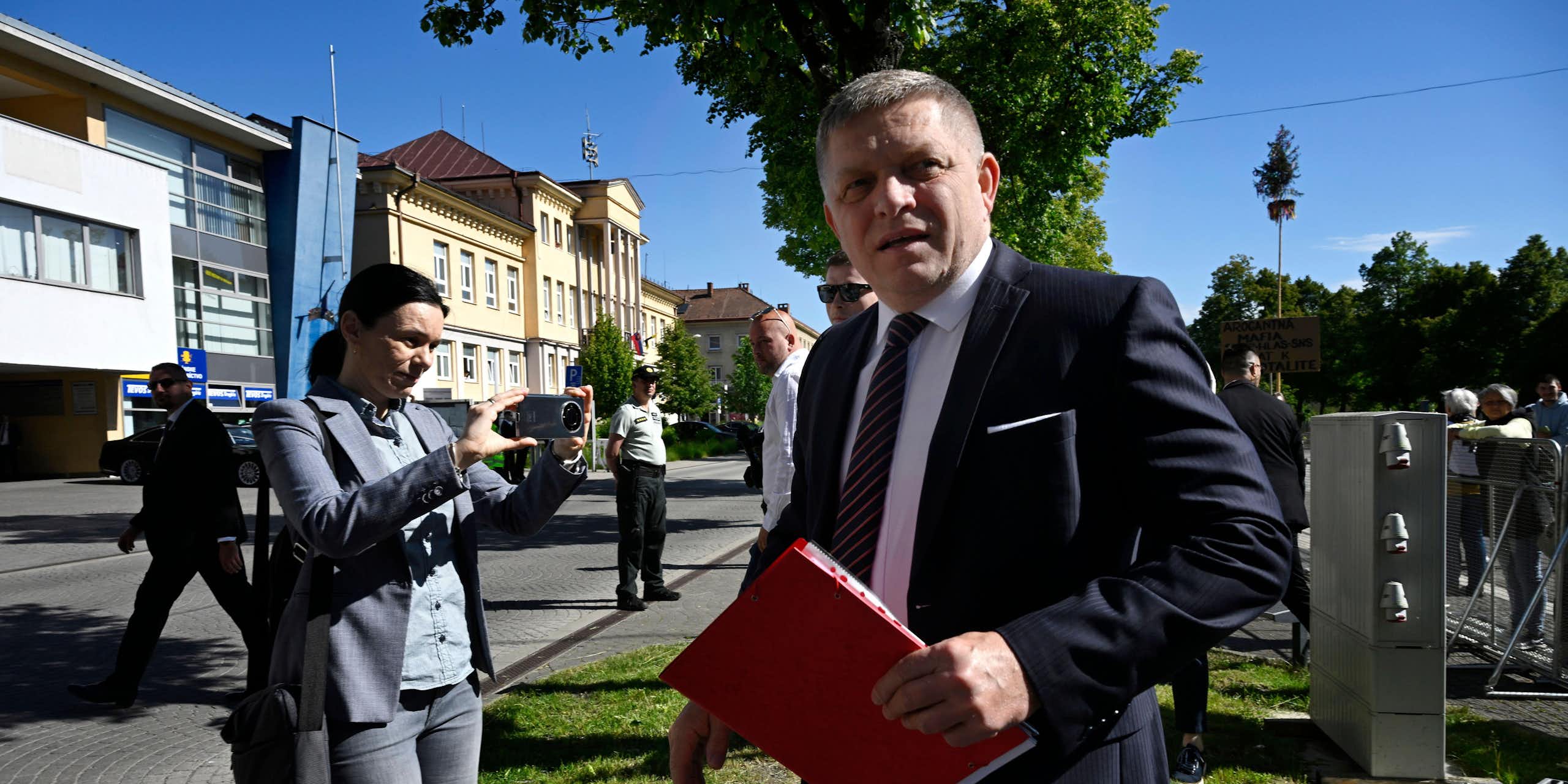 Robert Fico holding a binder of documents with security in the background.
