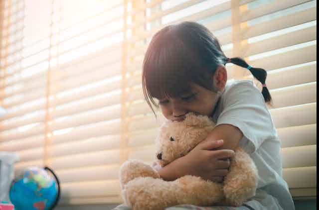 A sad little girl hugs her teddy bear.