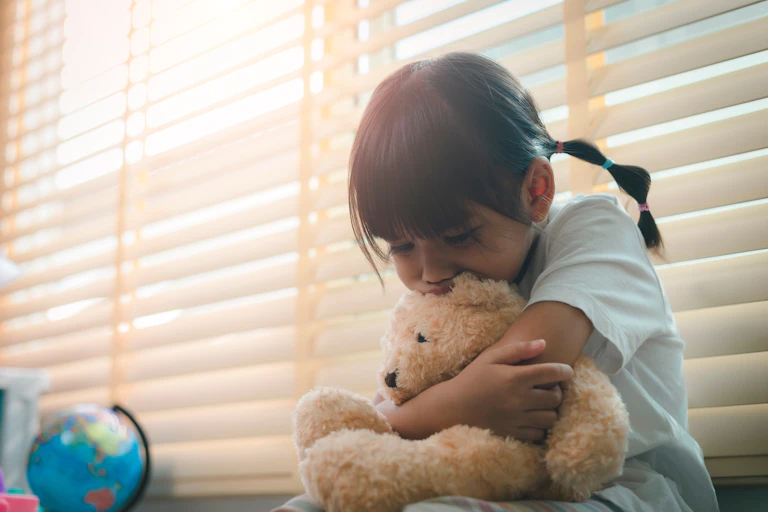 A sad little girl hugs her teddy bear.