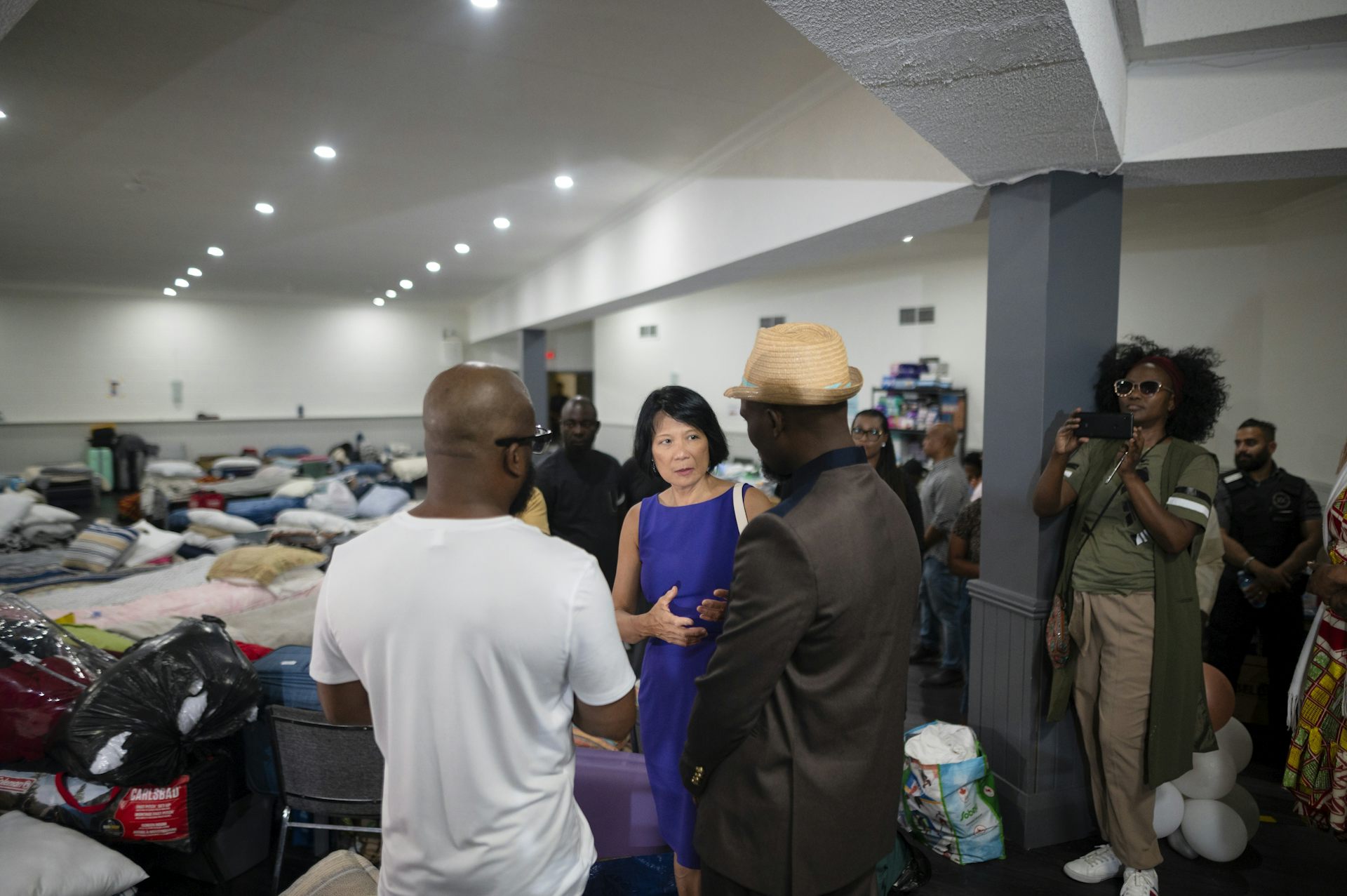 A woman in a suit seen speaking with people in a room with cots.