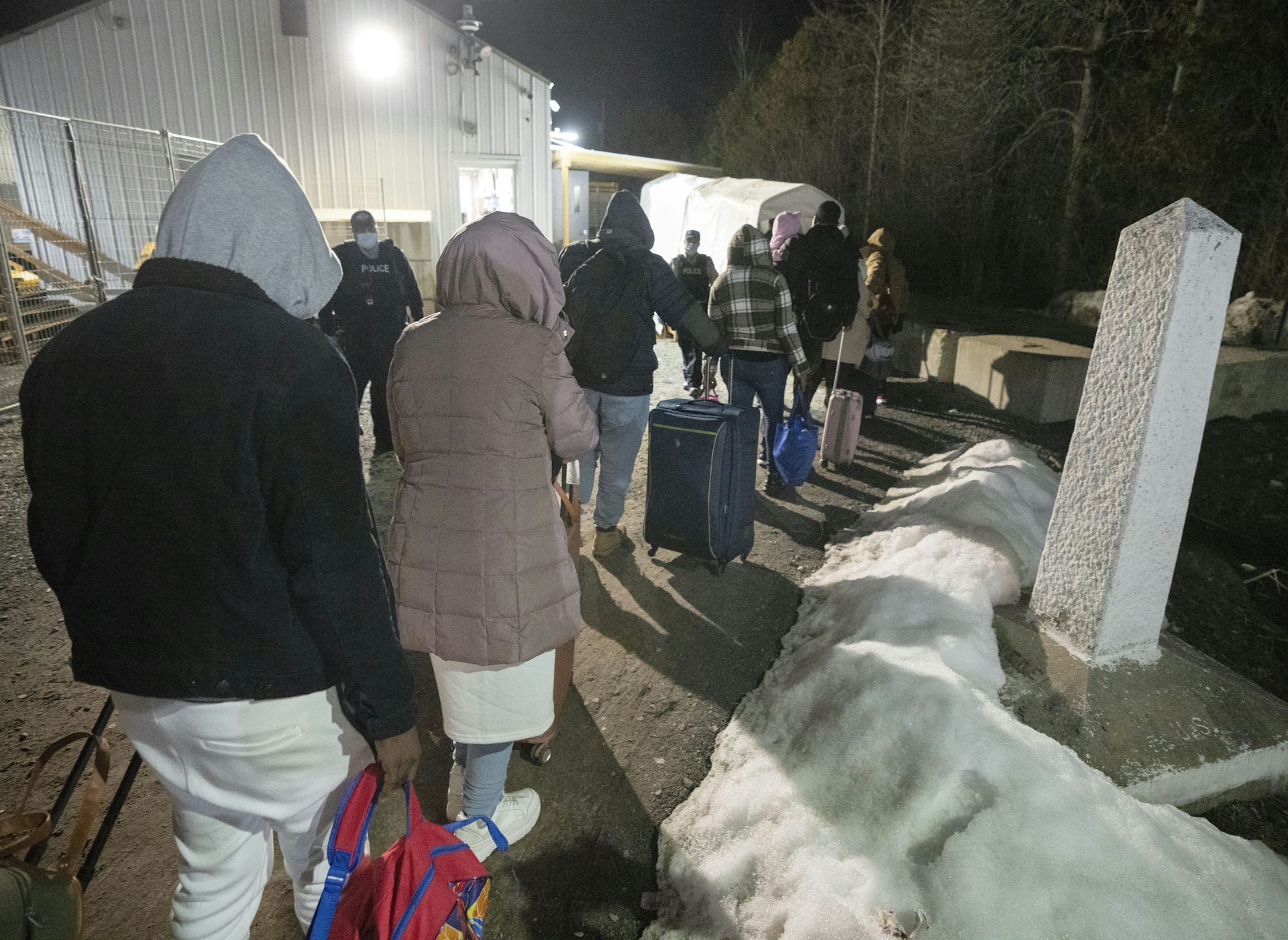 The backs of people with luggage at a border checkpoint.