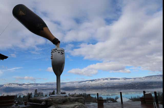 A statue of a wine glass and bottle is seen against a large valley.