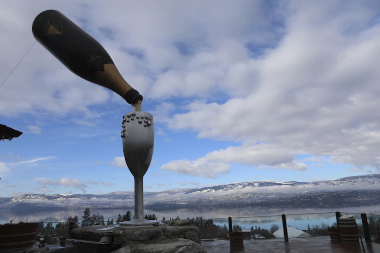 A statue of a wine glass and bottle is seen against a large valley.
