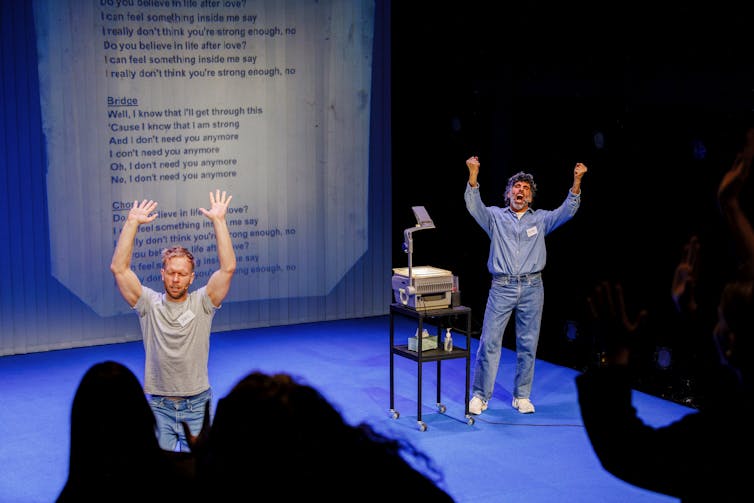 Two men on stage, lifting up their arms.