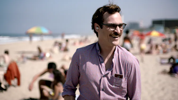 Photo of a man at the beach, wearing an earpiece, glasses and with a device in his shirt pocket.
