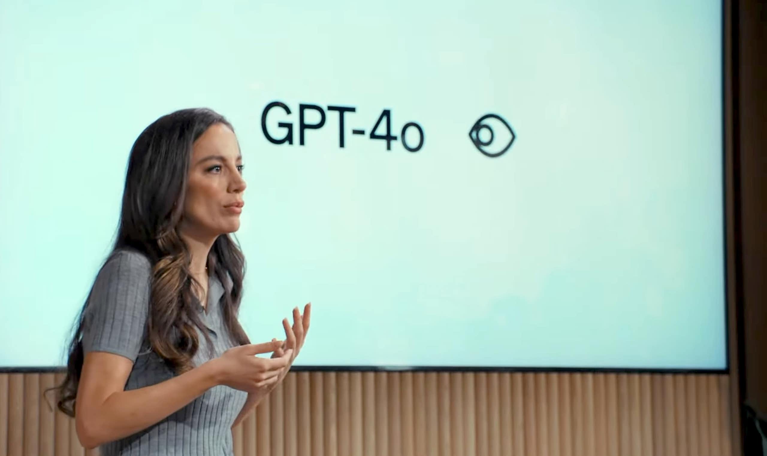 A photo of a woman talking in front of a screen showing 'GPT-4o'.
