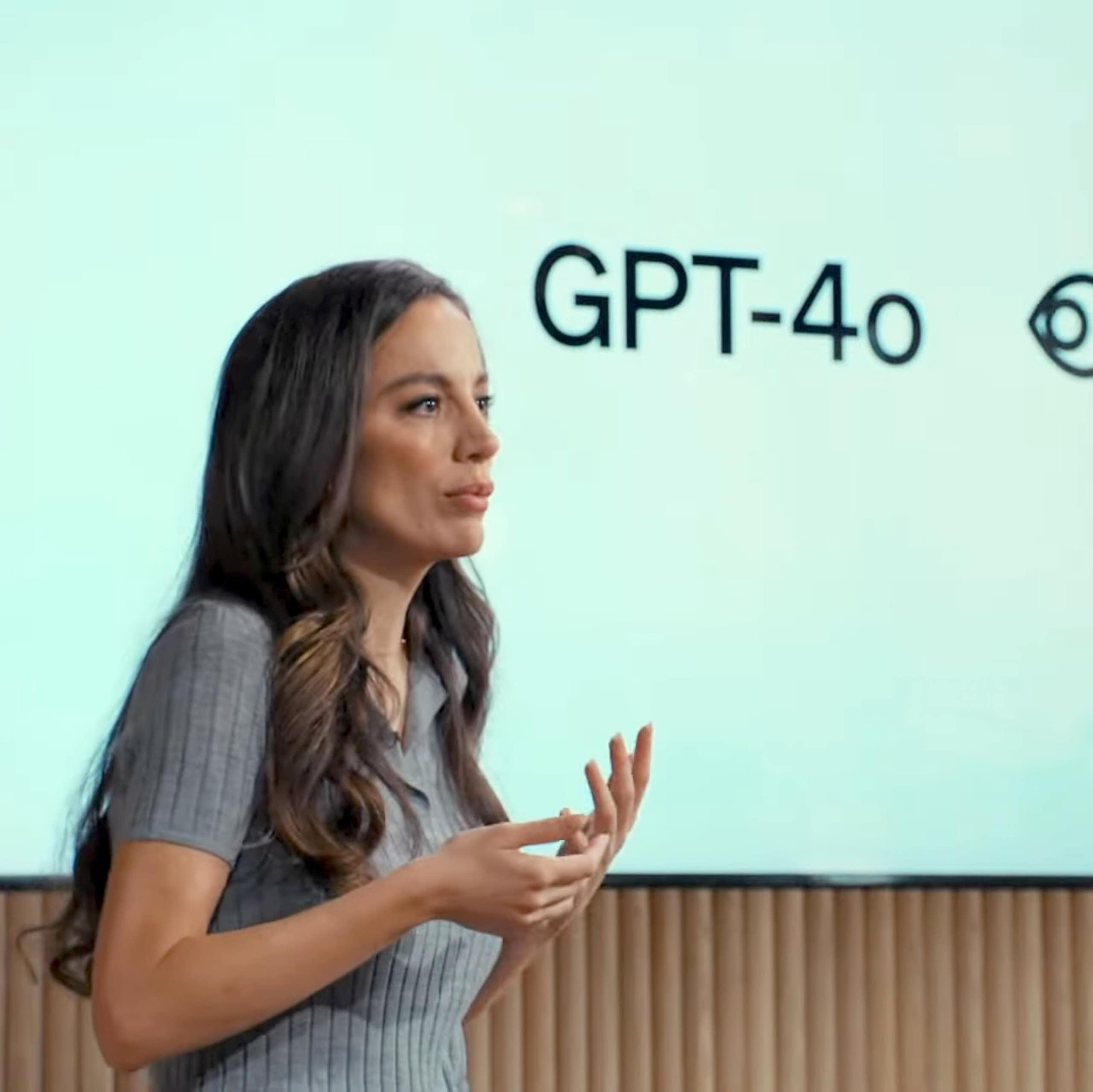 A photo of a woman talking in front of a screen showing 'GPT-4o'.
