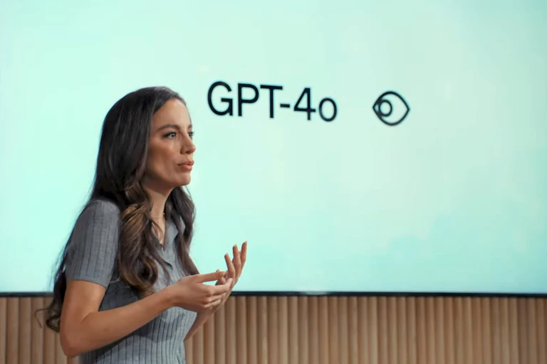 A photo of a woman talking in front of a screen showing 'GPT-4o'.