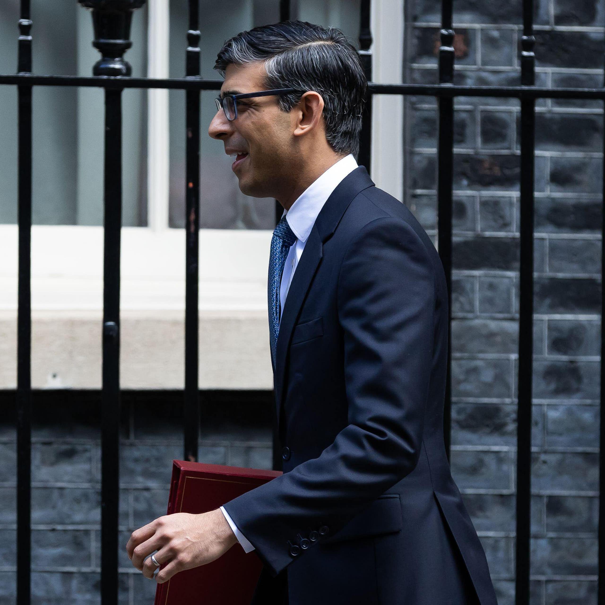 Side view of prime minister Rishi Sunak walking in front of Downing Street, holding a red ministerial folder under his arm