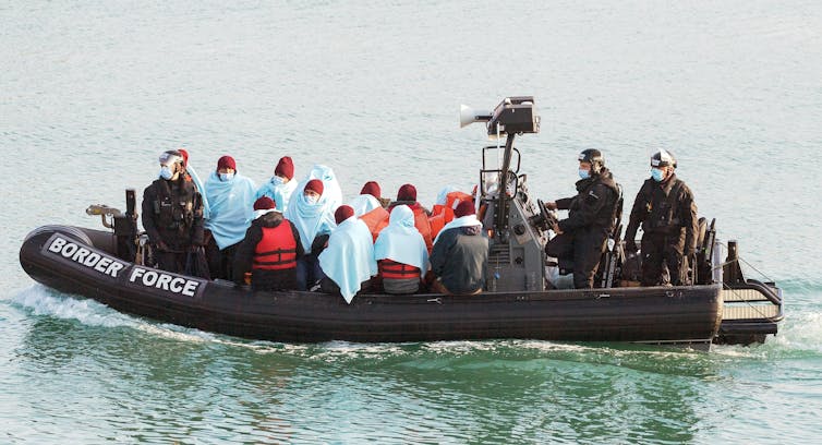 A UK border force branded dinghy full of people wrapped in blankets and hats
