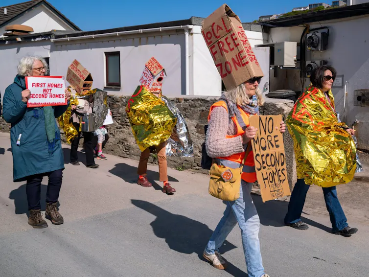 People wearing emergency blankets protest with placards.
