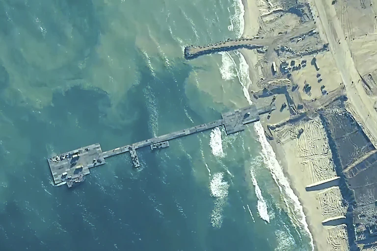 An overhead image shows a floating platform connected by a floating roadway to a beach.