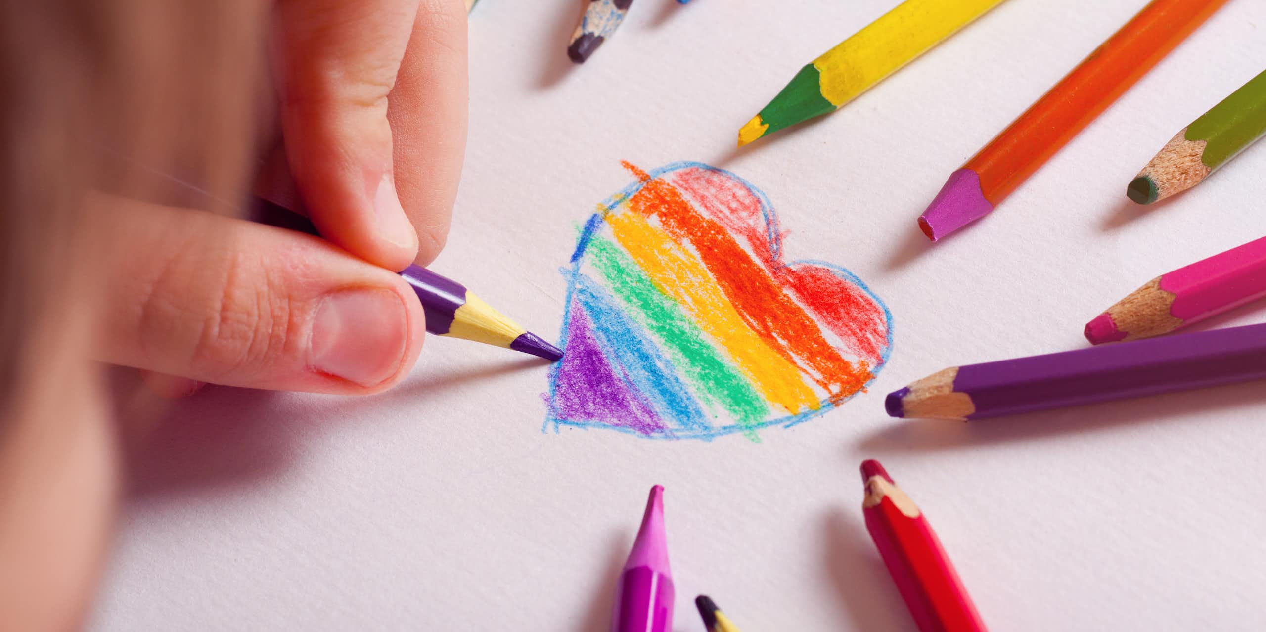 A kid drawing a heart with the LGBT-flag colours inside