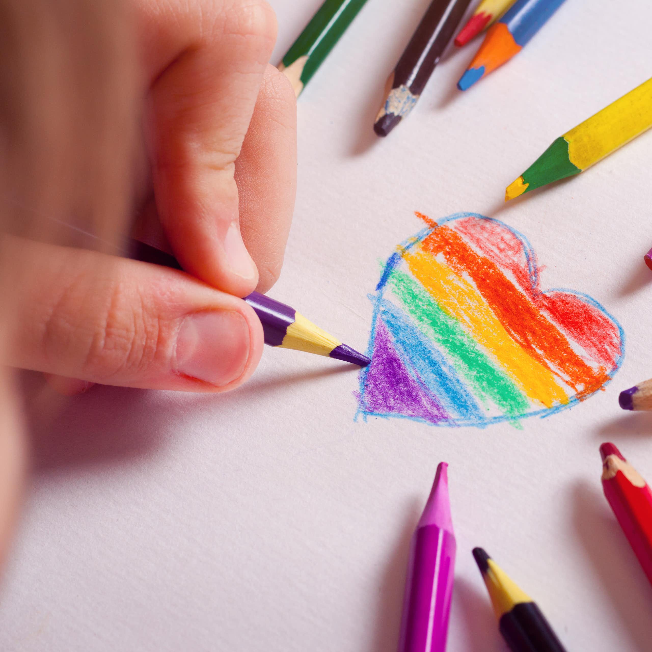 A kid drawing a heart with the LGBT-flag colours inside