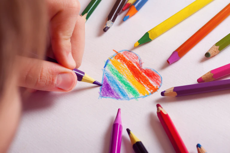 A kid drawing a heart with the LGBT-flag colours inside
