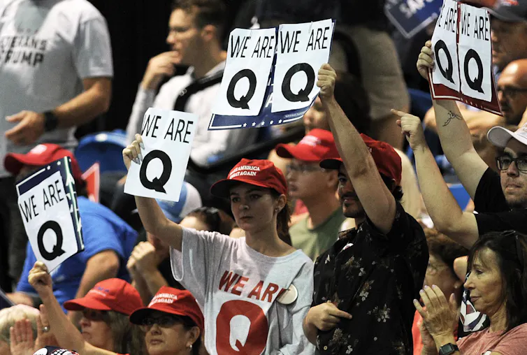 People holding up signs saying 'Q'.