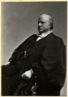 A bald man in a black robe and a white shirt with a stiff collar.