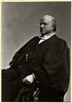 A balding man in a black robe and a white, stiff-collared shirt.