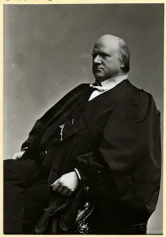 A balding man in a black robe and a white, stiff-collared shirt.