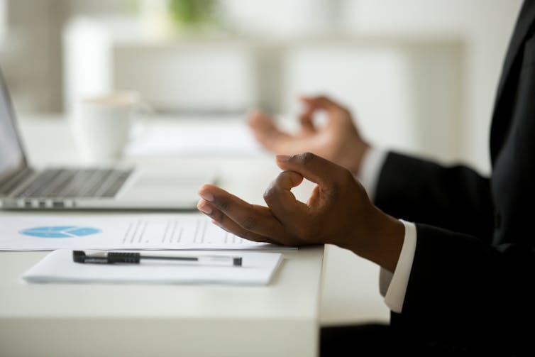 Close up of a pair of hands resting on a desk. The index finger and thumb are touching, while the remaining three fingers are straight.