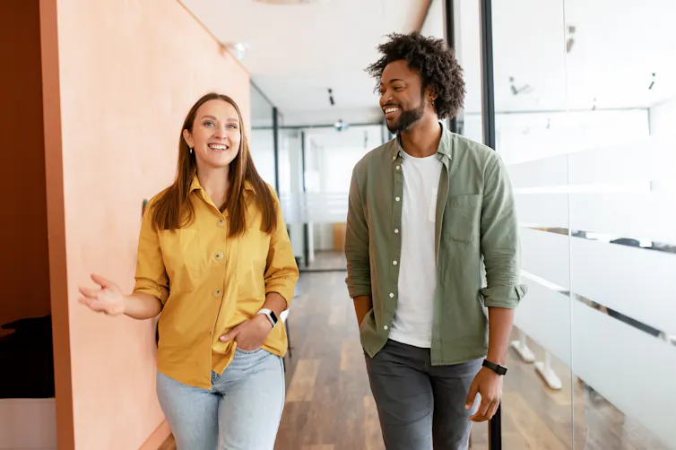 A young man and a young woman walk side-by-side down a hallway while having a conversation