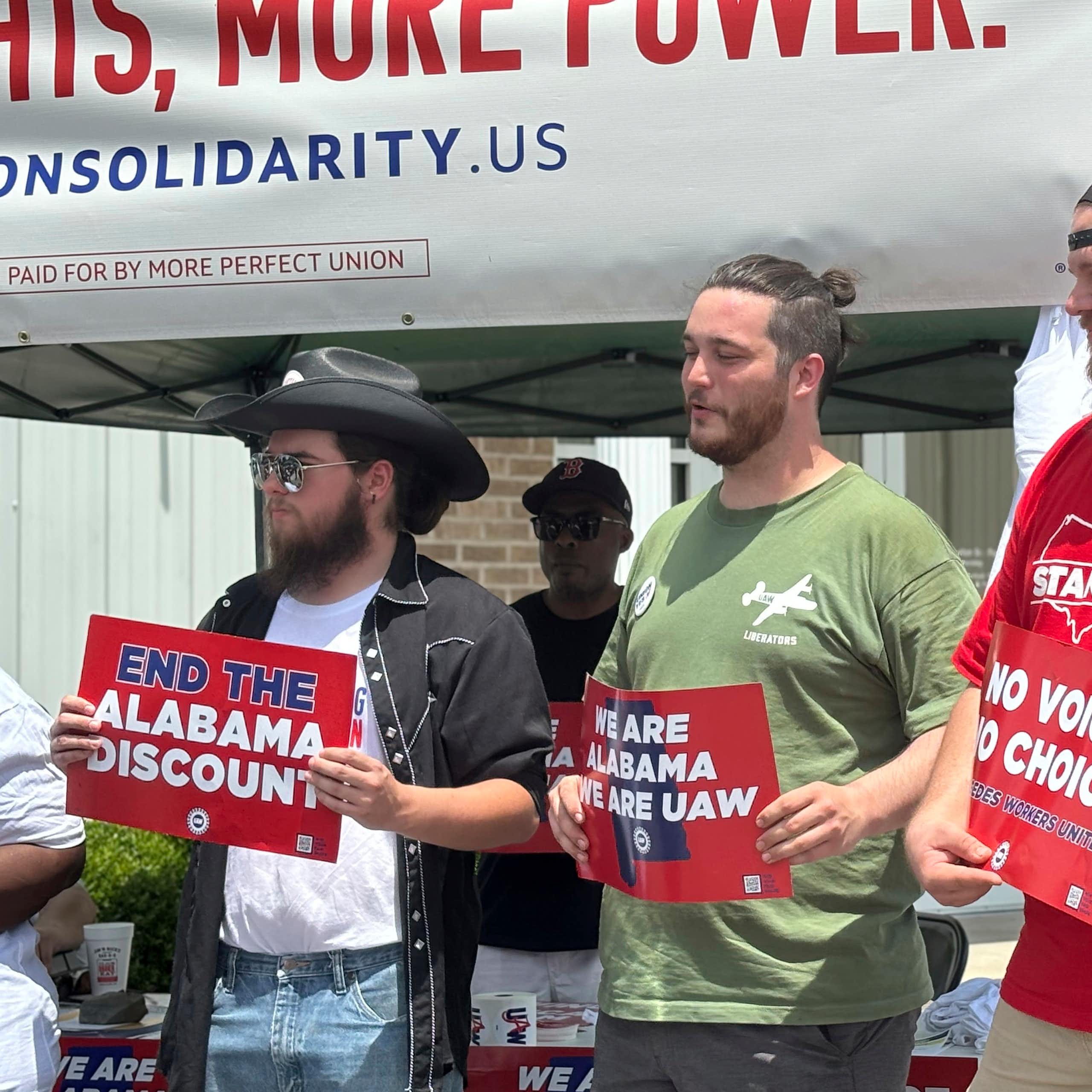 Three men hold signs in favor of the UAW and worker rights.