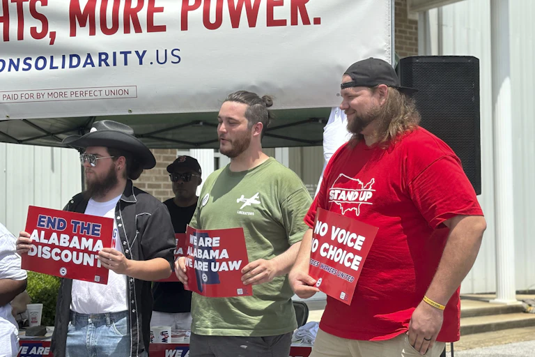 Three men hold signs in favor of the UAW and worker rights.