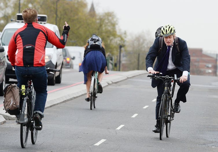 Um homem mostra o dedo do meio para Boris Johnson enquanto eles passam de bicicleta.