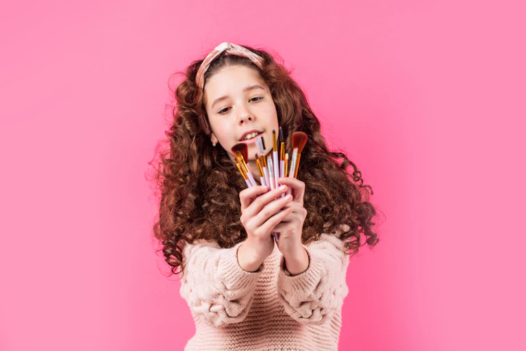 Une enfant tient devant elle des pinceaux et crayons à maquillage