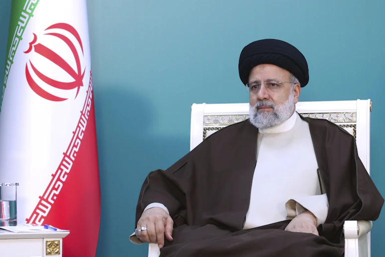 A man in traditional Iranian dress sits on a chair.