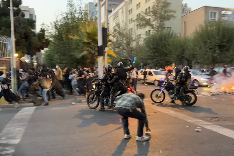 Police officers on motorcycles swing a baton as a group of protesters disperse.