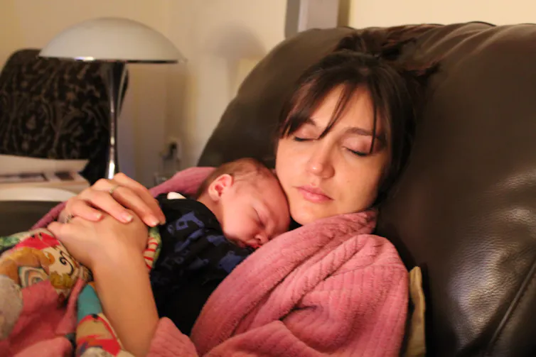 A mother lying on a couch with her newborn baby.