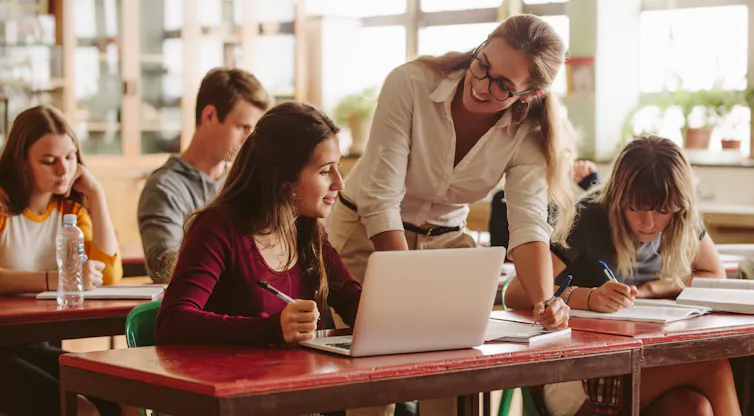 A female teachers chats happily to a teenage girl student in a classroom.