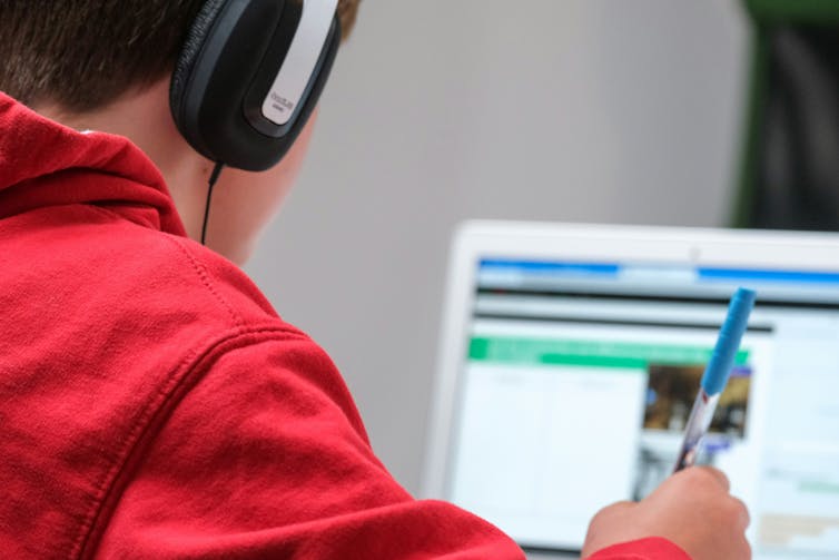 boy sits at laptop wearing headphones