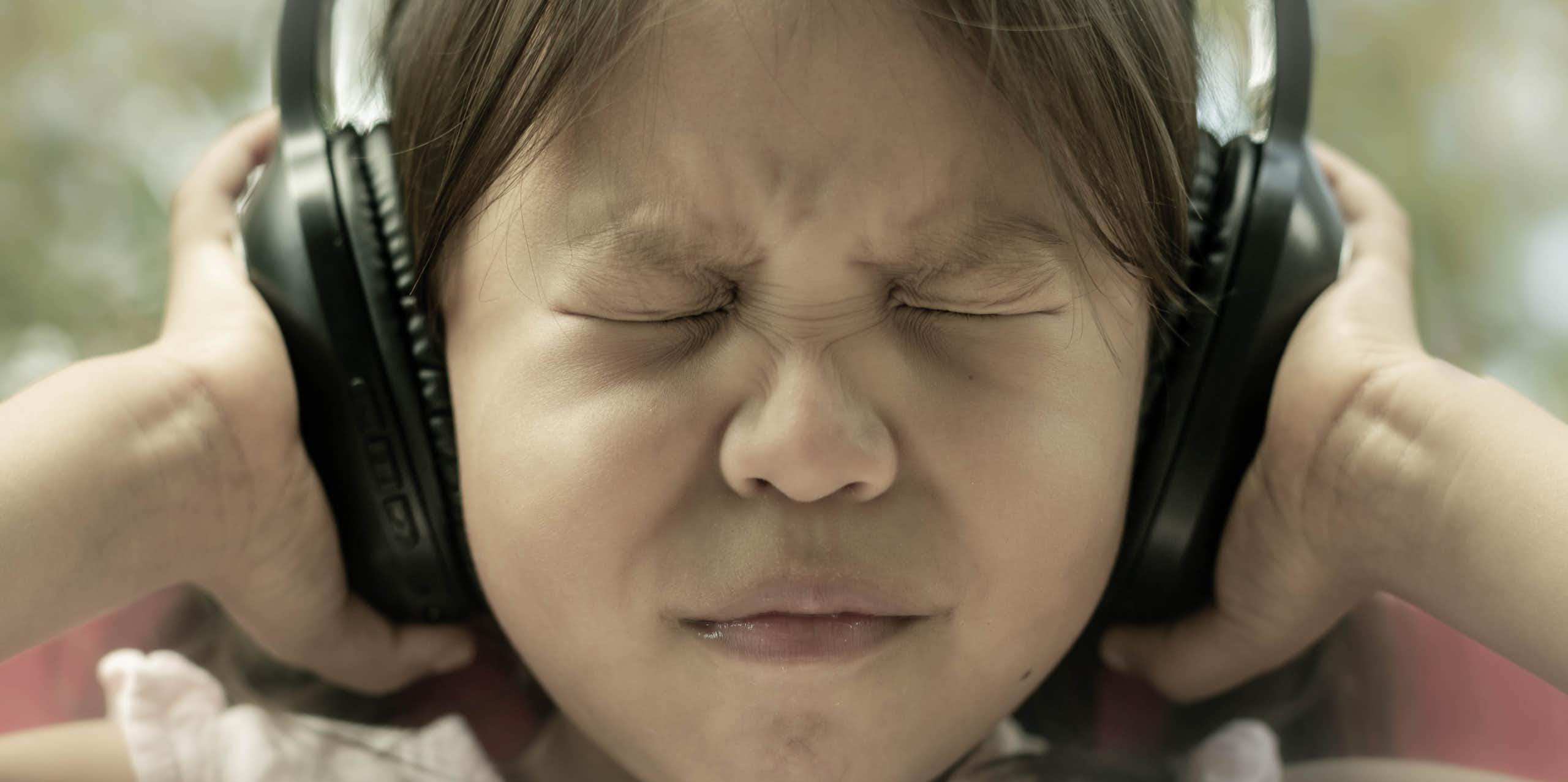 girl shuts eyes tightly and pushes headphones against ears