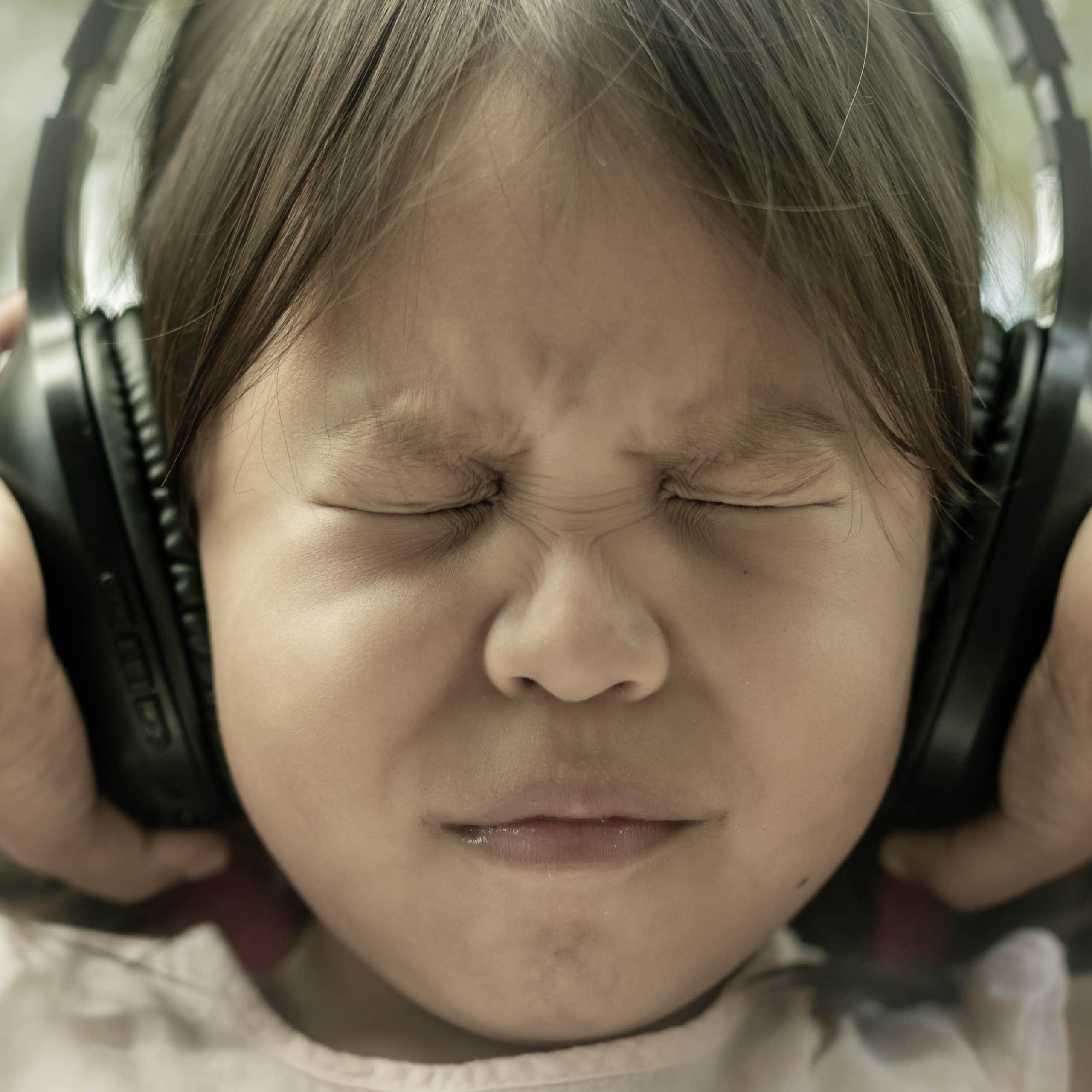 girl shuts eyes tightly and pushes headphones against ears