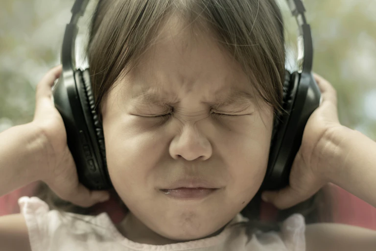 girl shuts eyes tightly and pushes headphones against ears