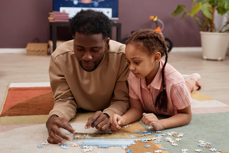 Dad and daughter solving jigsaw puzzle while laying on floor