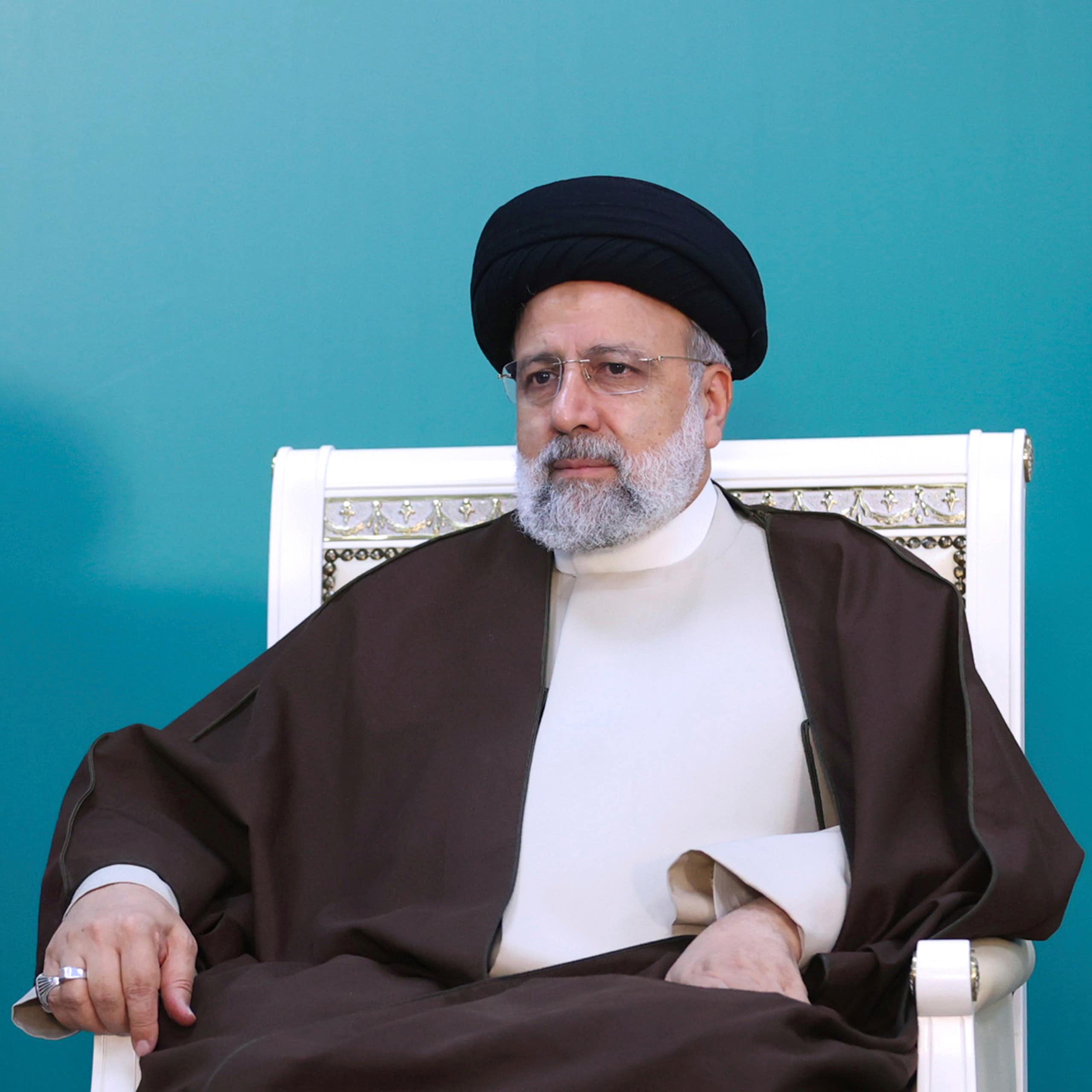 Un hombre vestido con el traje tradicional iraní sentado en una silla.