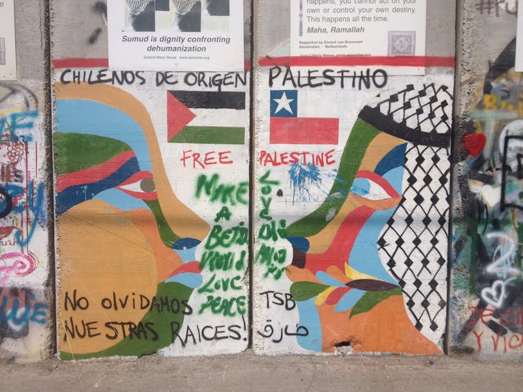 El graffiti en una pared muestra a dos hombres mirándose fijamente, una bandera chilena al lado y una bandera palestina en la otra.